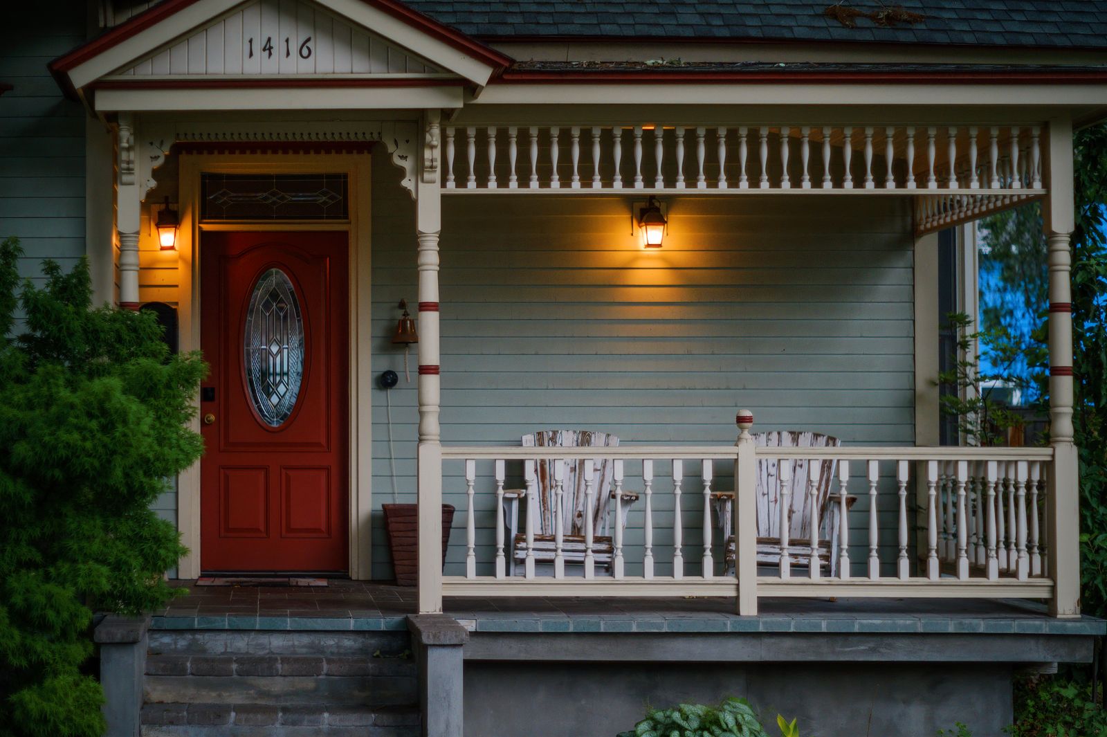 Inviting porch with red door, wooden armchairs, and glowing lights, perfect for evening relaxation.